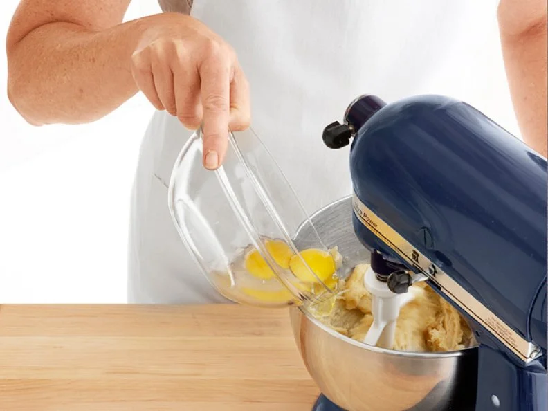Eggs Being Pouring from a Glass Mixing Bowl into an Operating Mixers Bowl
