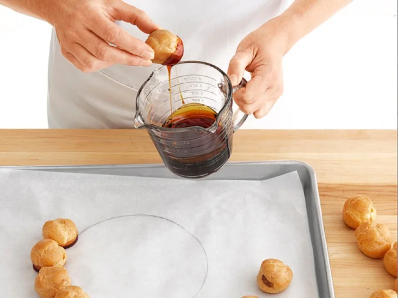 A Round Pastry Being Dipped Into Caramel in a Measuring Cup