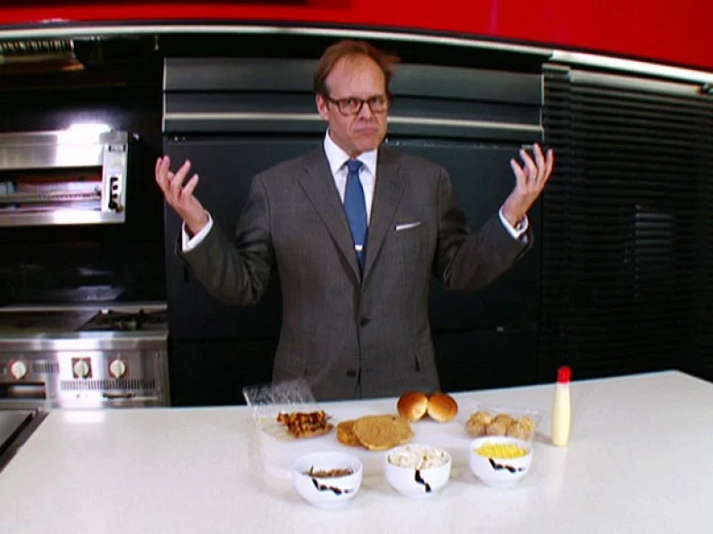 Alton Brown with a perplexed look on his face and  his hands raised