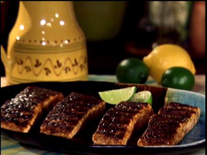Four pieces of grilled salmon with a dry rub on a plate with two lime wedges