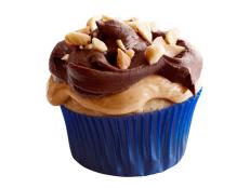 A cupcake topped pieces of nuts and swirls of peanut butter and chocolate 