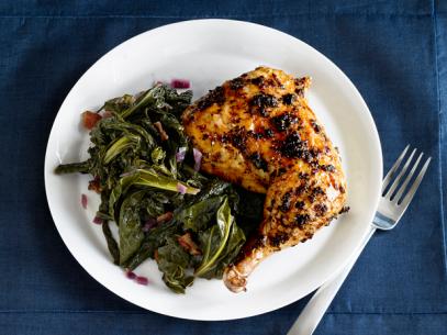 A piece of roasted chicken on a plate with greens