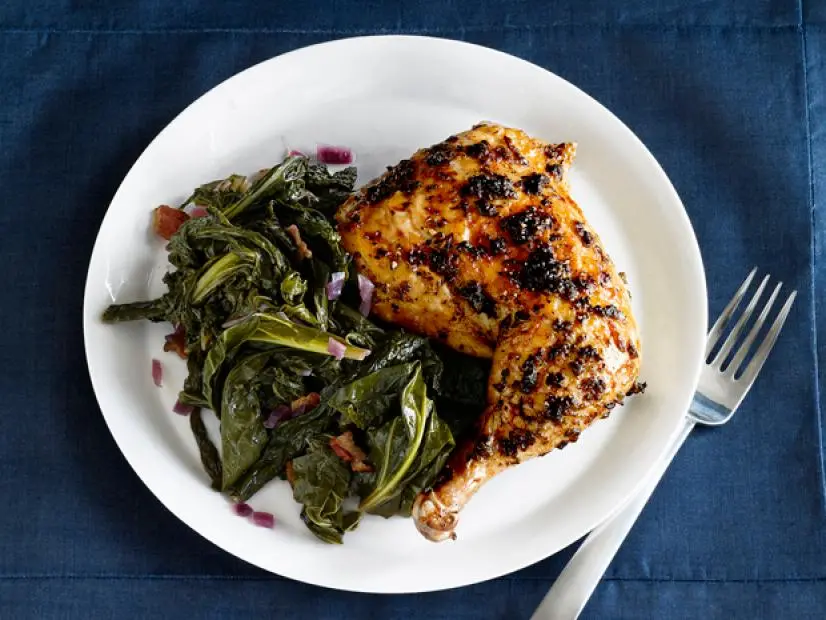 A piece of roasted chicken on a plate with greens