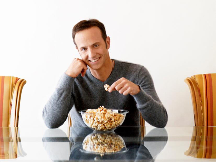 Brian Boitano sitting at a glass table eating popcorn