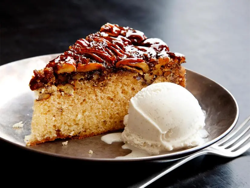 A slice of cake with a pecan top beside a scoop of vanilla ice on a plate