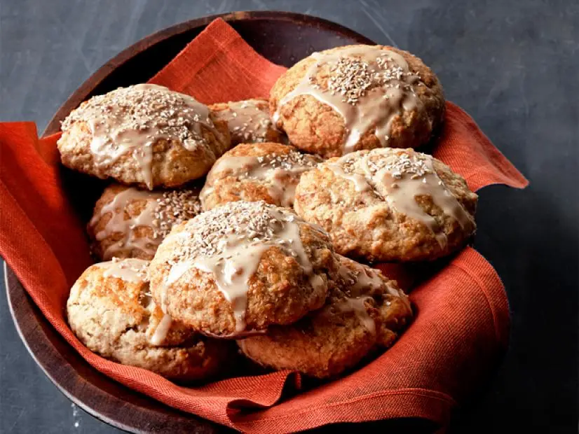 A wooden bowl containing a pastry with frosting drizzles on top of them