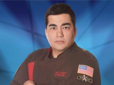 Jose Garces against a blue background wearing a brown and red chefs uniform