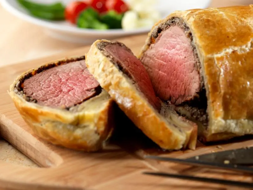 A sliced beef wellington on a wooden cuttingboard