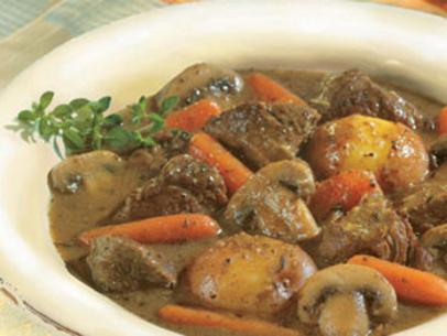 A Bowl of Beef Stew with carrots, Potatoes, herbs and mushrooms in a white bowl