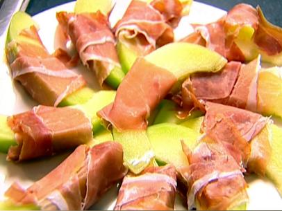 A platter with pieces of galia melon wrapped with slices of prosciutto.