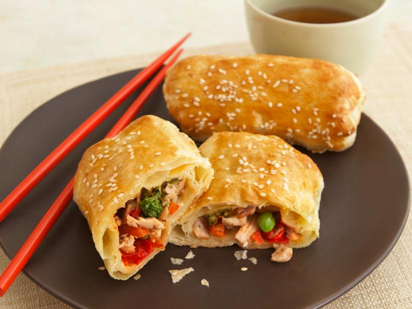 Two Chinese Egg Rolls Beside Red Chopsticks on a Round Brown Plate
