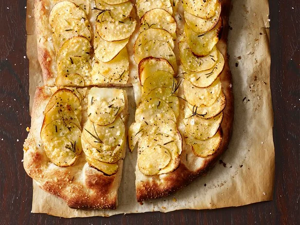 A flat bread with a sliced vegetable and herbs on a brown piece of paper