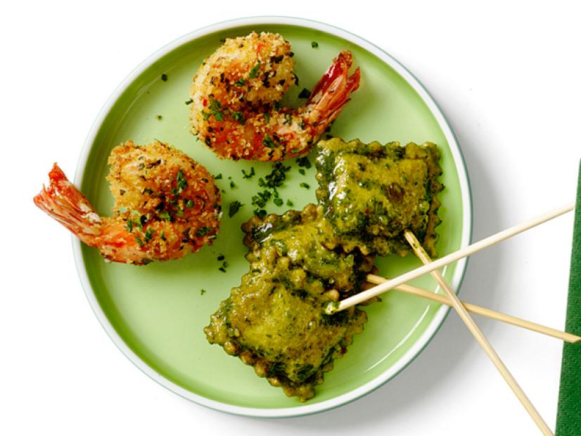 Three raviolis on skewers and two shrimps placed on a small green plate