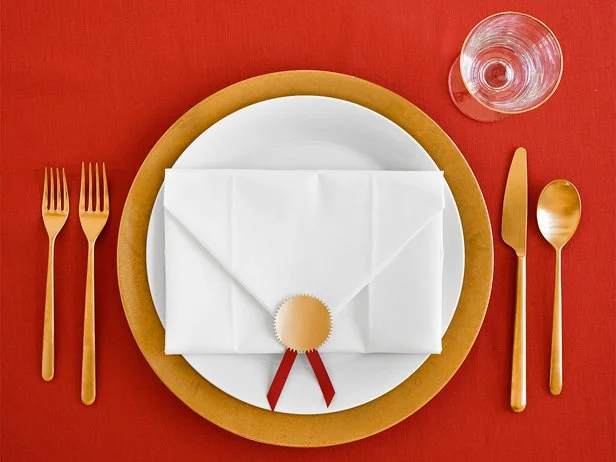 A place setting made of a white plate trimmed in gold, gold cutlery and a clear glass