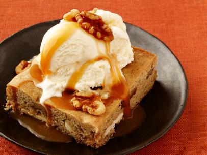 A slice of cake topped with vanilla ice cream, walnuts and caramel on a small brown plate