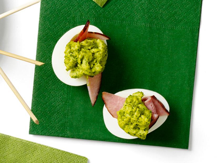 Two deviled eggs filled with ham and a green mixture placed on a dark green napkin