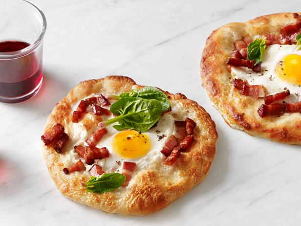 Two breakfast pizzas an small glass of juice on a marble surface