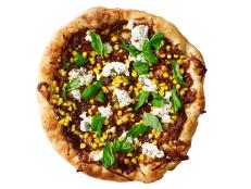 A pizza topped with corn, cheese and greens