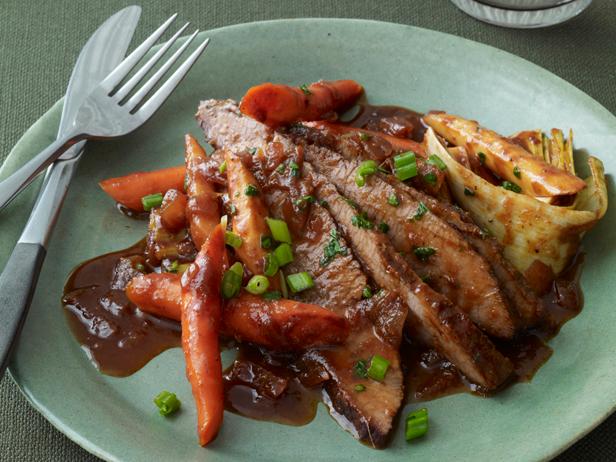 Sliced brisket topped with gravy on a green plate with carrots