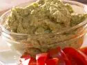 a bowl of hummus in a glass bowl beside slices of red bell peppers