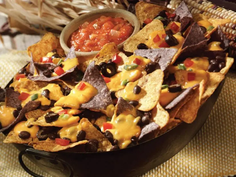 Deluxe Nachos made of two different tortillas with a side of salsa in a black pan