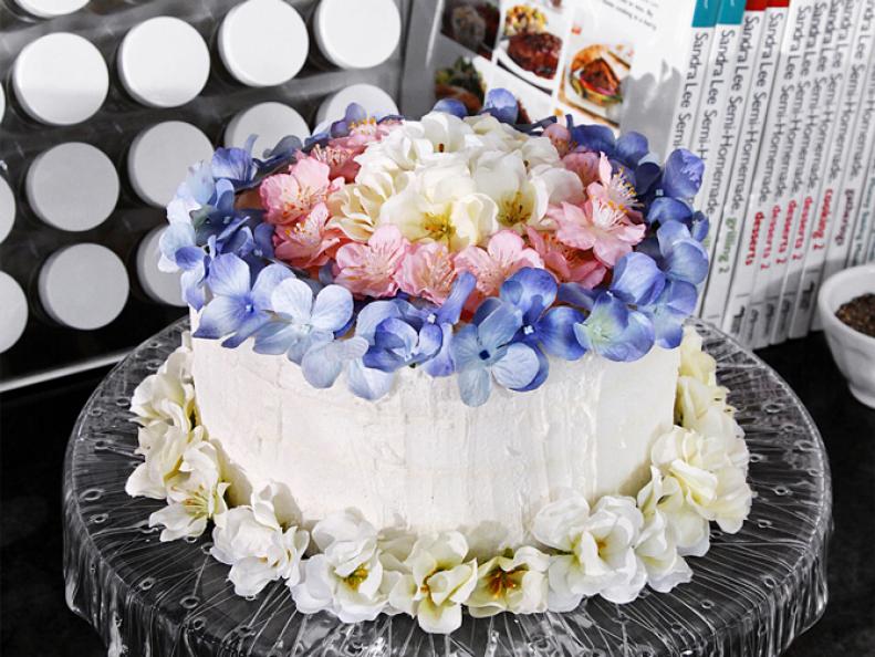 A cake with white icing decorated with white, purple and pink flowers