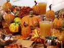A table is set for the Thanksgiving holiday with a pumpkin patch centerpiece with serveral different pumpkins and place settings of fall color.