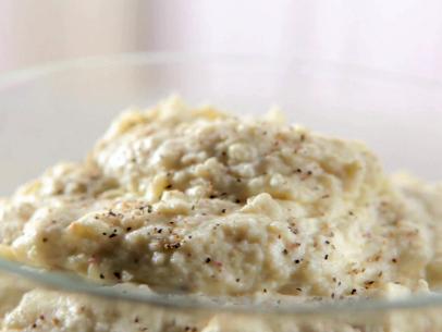 Peppered goat cheese mashed potatoes with a sprinkle of pepper in a glass serving bowl.