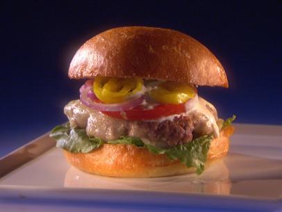 A Greek burger topped with tomoto, cheese, red onions and banana peppers on a thin gray square plate 
