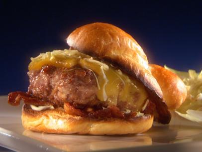 A smoked pig burger on a bun with bacon, and topped with cheese that is placed on a thin gray square plate