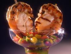 Shrimp wrapped around scallops on skewers a top muliti-colored salsa in a margarita glass