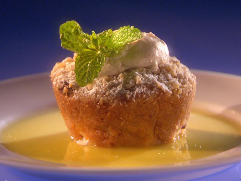 Apple Bread Pudding topped with cream and a mint sprig while sitting in a pool of yellow sauce on a small white plate