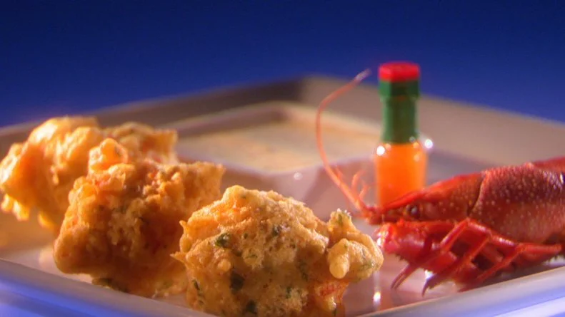 Crawfish beignets, a small whole lobster and a miniature bottle of hot sauce on a thin gray square plate