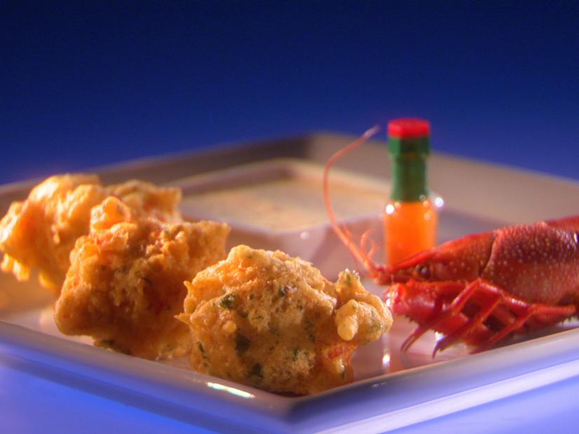 Crawfish beignets, a small whole lobster and a miniature bottle of hot sauce on a thin gray square plate