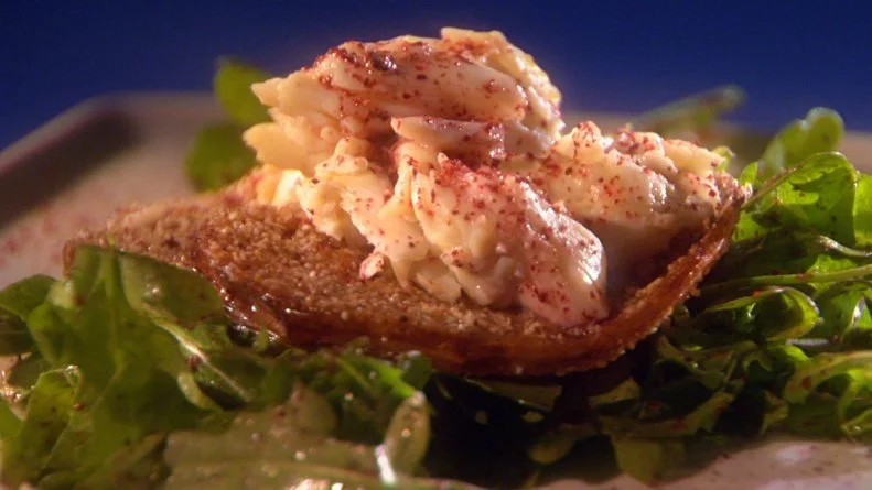 A seasoned crab mixture a top a bed of greens on a thin gray square plate