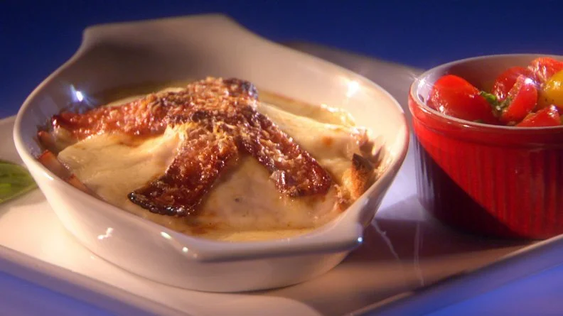 A sandwich smothered in sauce and topped with gravy next to a red dish of mixed fruit