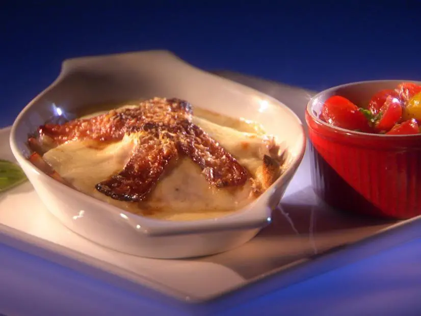 A sandwich smothered in sauce and topped with gravy next to a red dish of mixed fruit