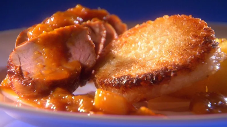 Slices of pork, grilled pineapple and a mango sauce on a plain white plate