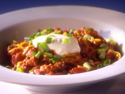 Chili topped with whipped cream and chives in a plain white bowl
