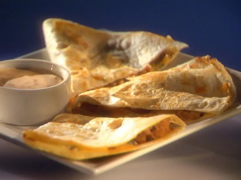 A cut Turkey Quesadilla on a plate with a container of sauce