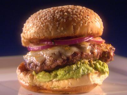 A Cemita Burger on a bed of guacamole and topped with cheese and purple onions