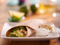 A Chicken and Bean Burrito on a square plate along side two clear containers of sauce