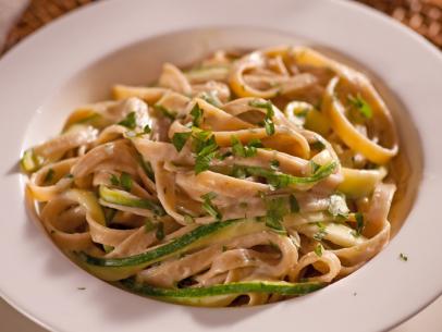 Fettuccini Alfredo with slices of zucchini and chopped herbs in a plain white bowl