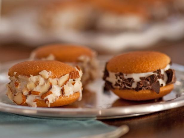 Three mini ice cream sandwiches encrusted with chopped nuts or chocolate bits of chocolate on a small dish