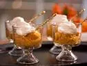 Pumpkin Rice Pudding with whipped topping in small glass dessert dishes and gold spoons sticking in them