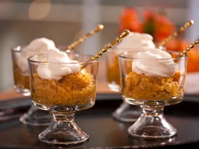 Pumpkin Rice Pudding with whipped topping in small glass dessert dishes and gold spoons sticking in them