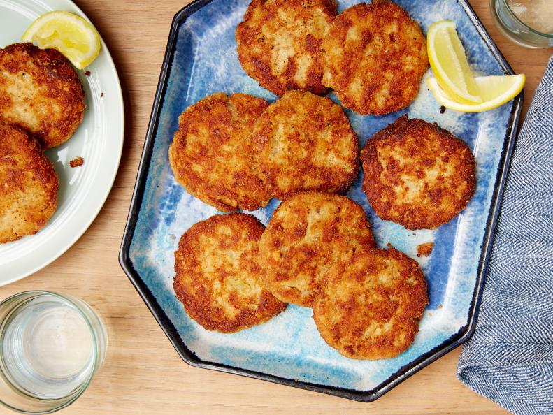 Two rows of Salmon Cakes on a plate next a whole lemon and a dish of yellow sauce 