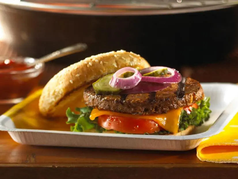 A regular burger on a bed of lettuce, cheese and tomatoes and topped with red onions and pickles