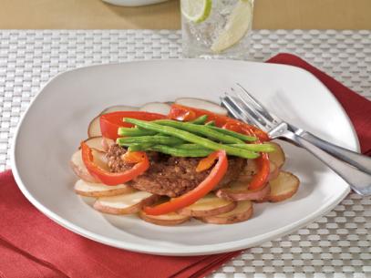 A veggie burger on sliced potatoes and topped with sliced red peppers and green beans