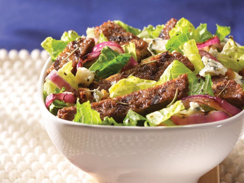 A salad consisting of lettuce,pieces of veggie burger and red onions in a plain white bowl